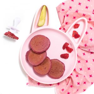 粉红色的兔子板或幼儿，里面装满了粉红色的煎饼，覆盆子和鳄梨，坐在粉红色的餐巾纸上，坐在带有白色叉子的粉红色餐巾纸上，供婴儿使用。