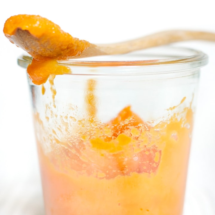 桃子和胡萝卜婴儿食品果泥在一个透明的罐子里，上面放着木勺。