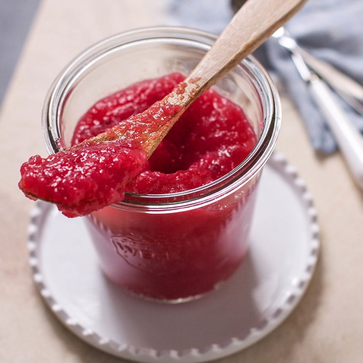 A glass jar of red beet applesauce with a small wood spoon.