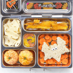 图像是一个开放的午餐盒，里面有健康的万圣节主题食物。