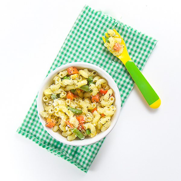 小白碗充满面食和蔬菜。坐在绿色和白色格仔的餐巾的顶部，用绿色和黄色的叉子装满了意大利面
