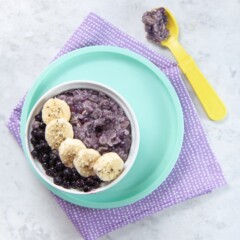 Bowl filled with blueberry oatmeal with slices of banana and frozen blueberries on top.GydF4y2Ba