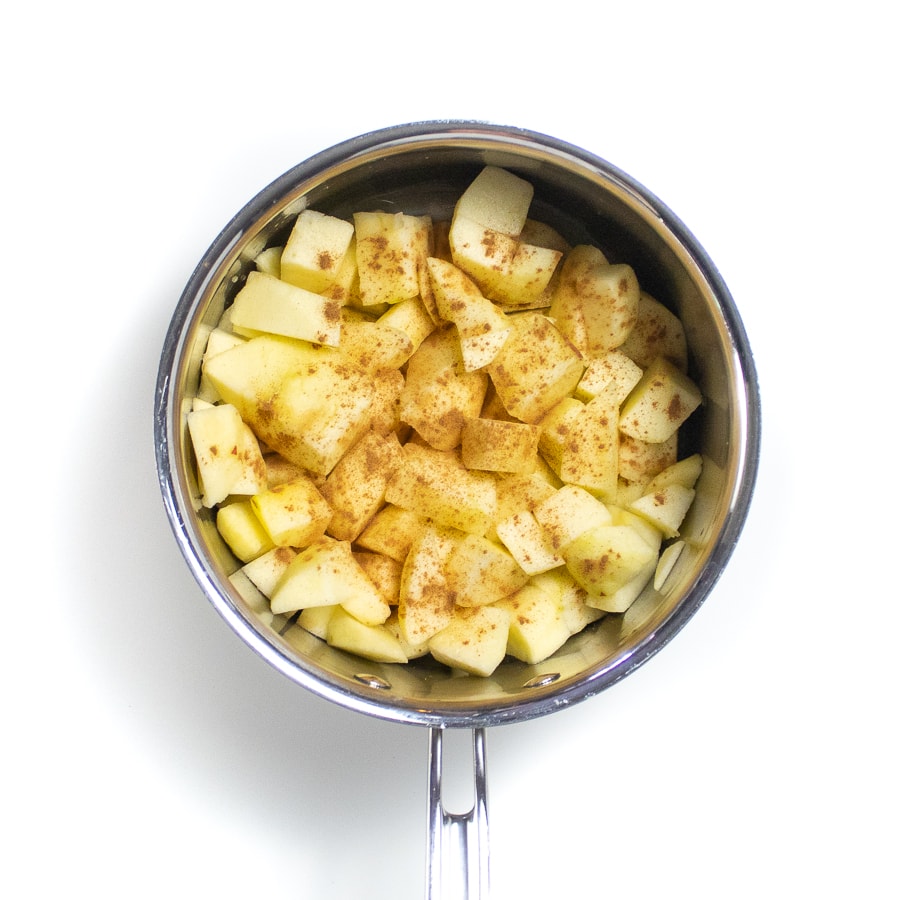 银酱锅在白色背景上，配以切碎的苹果，并撒上肉桂。