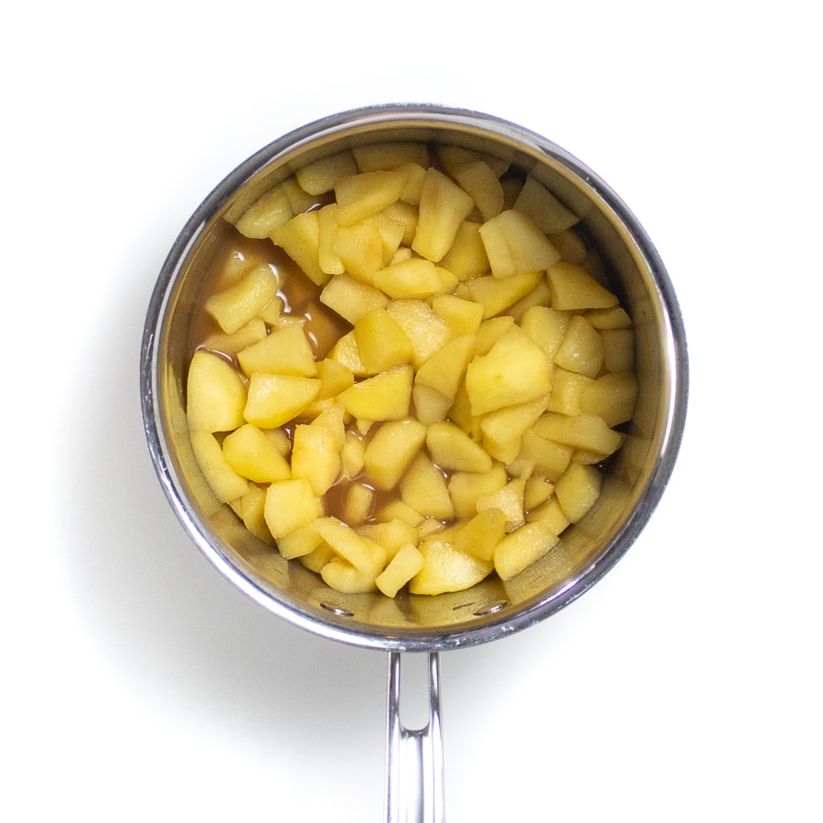 银酱锅在白色背景上，上面有煮熟的苹果。