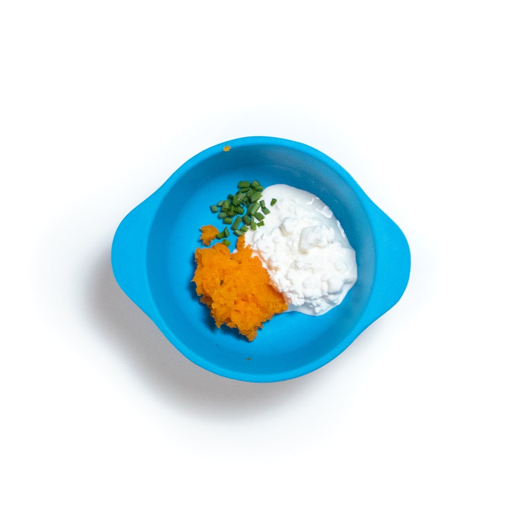 一个蓝色的婴儿碗，里面装满了土豆泥的胡萝卜奶酪和细香葱。