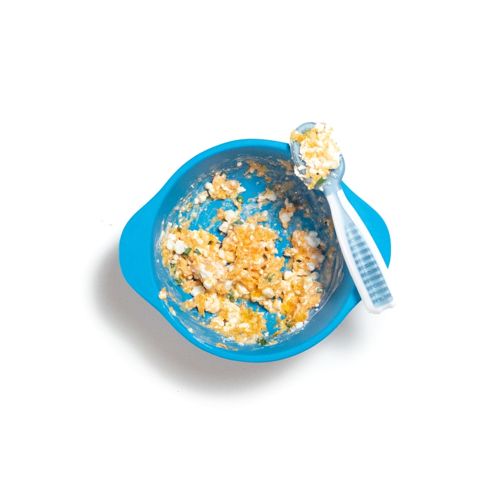 一个蓝色的婴儿碗，上面有土豆泥的胡萝卜，干酪和细香葱，边缘放在边缘。