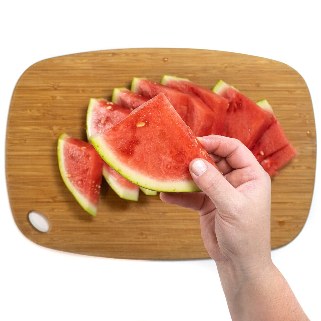 一只手在木制切菜板上拿着一片西瓜。