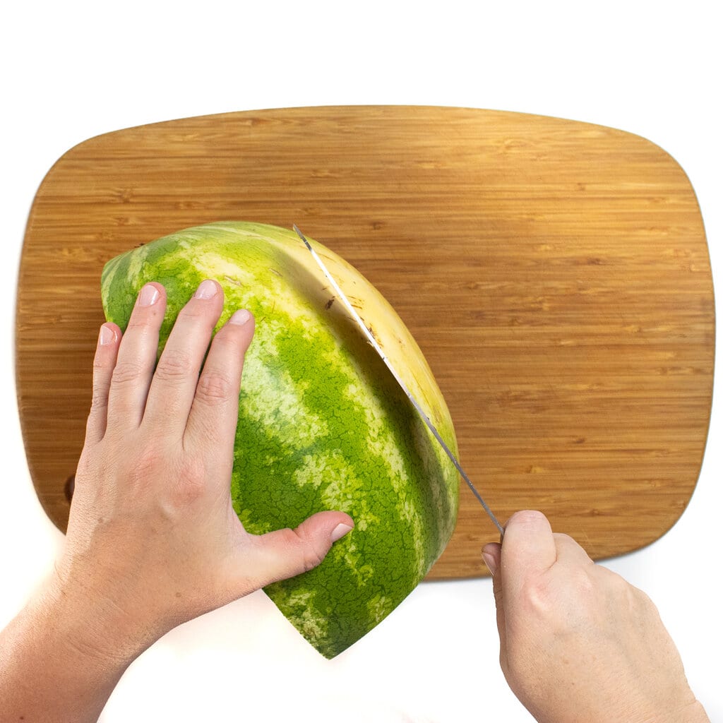 木制切菜板和西瓜和一只手握着刀切掉底部。