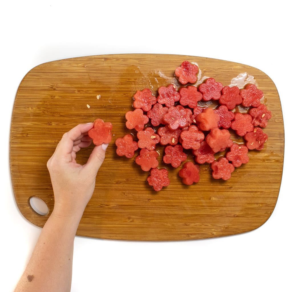 一只手拿着花形的西瓜块，用一堆花形的西瓜块在木制切菜板上