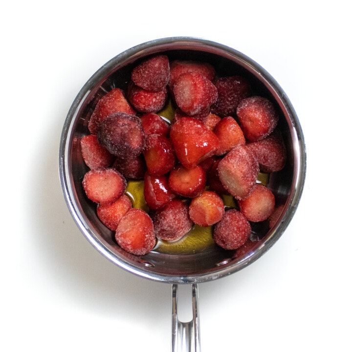 银酱锅在背景上充满冷冻草莓枫糖浆和香草提取物。