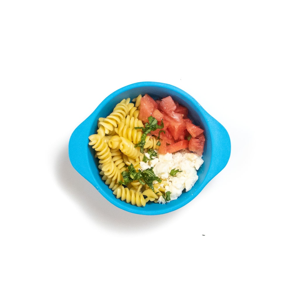 一个蓝色的婴儿碗，里面装有意大利面，罗勒，羊乳酪和西瓜。