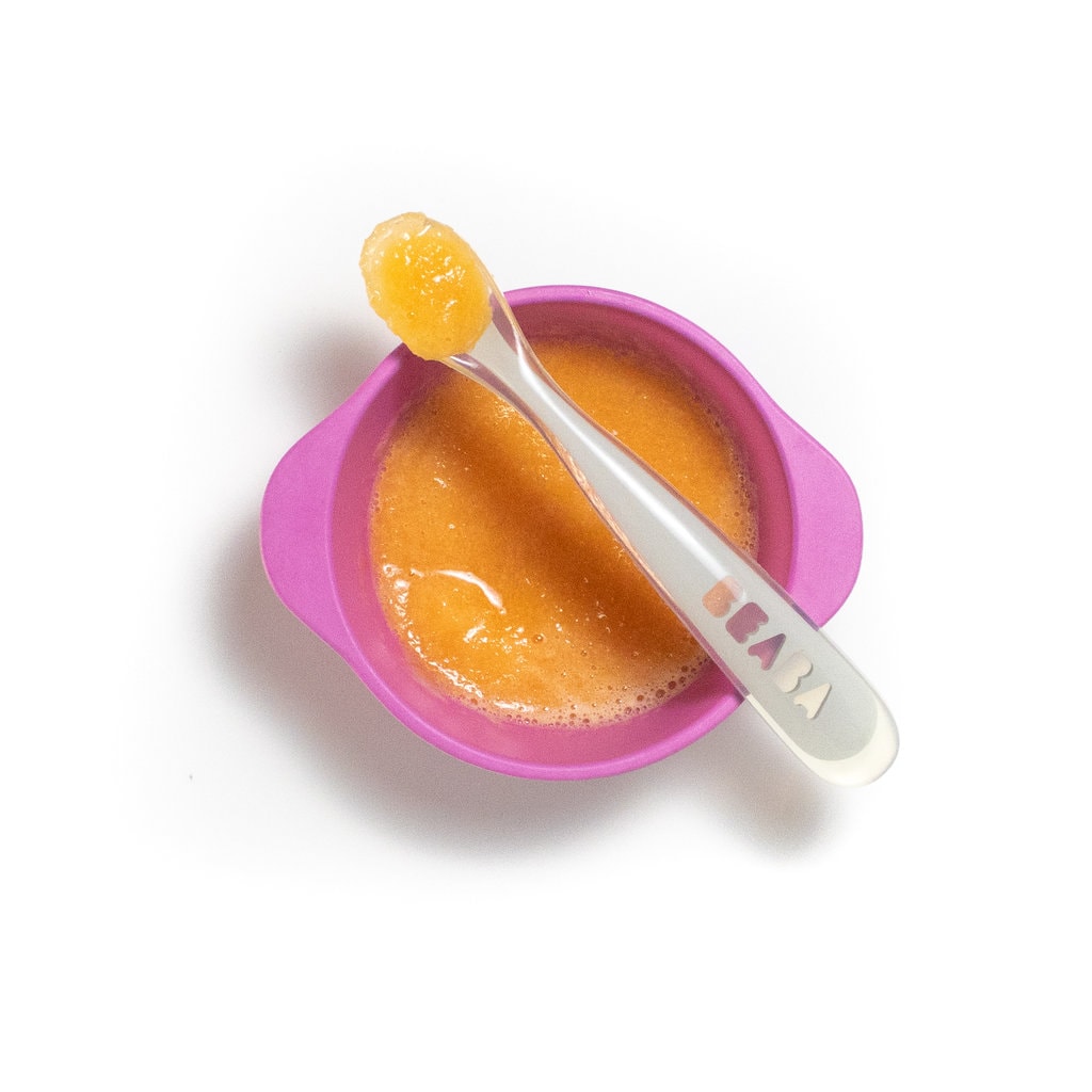 一个粉红色的婴儿碗，上面放着一块汤匙，上面放着勺子。