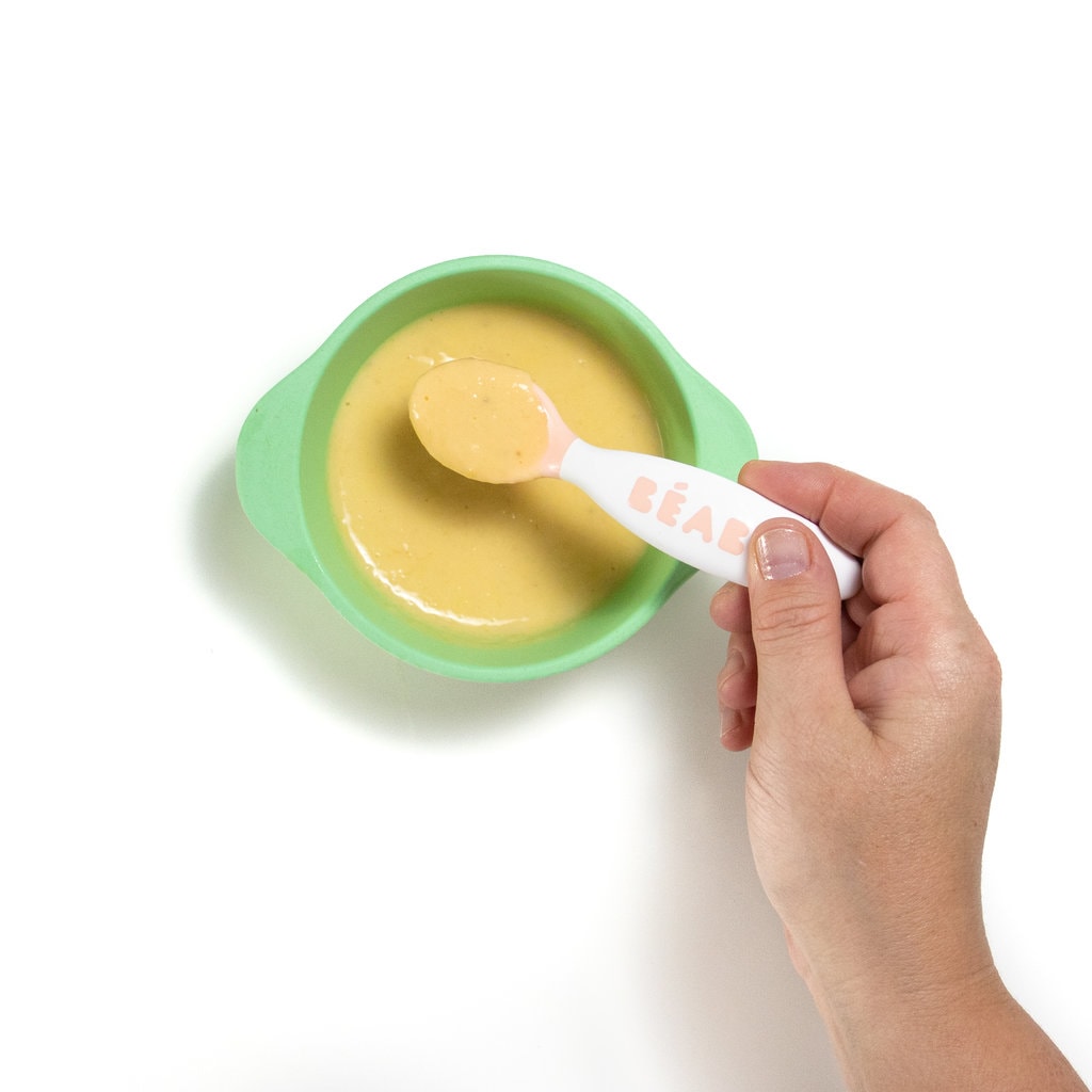 一个蓝绿色的婴儿碗，握着一把婴儿勺子搅动哈密瓜，酸奶和香蕉菜。