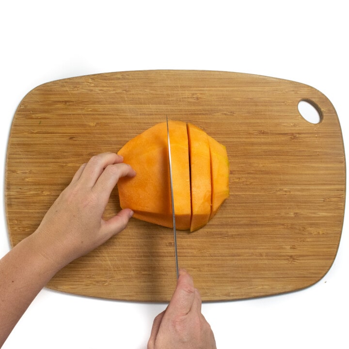 一个木制切菜板，用手切厚的哈密瓜。
