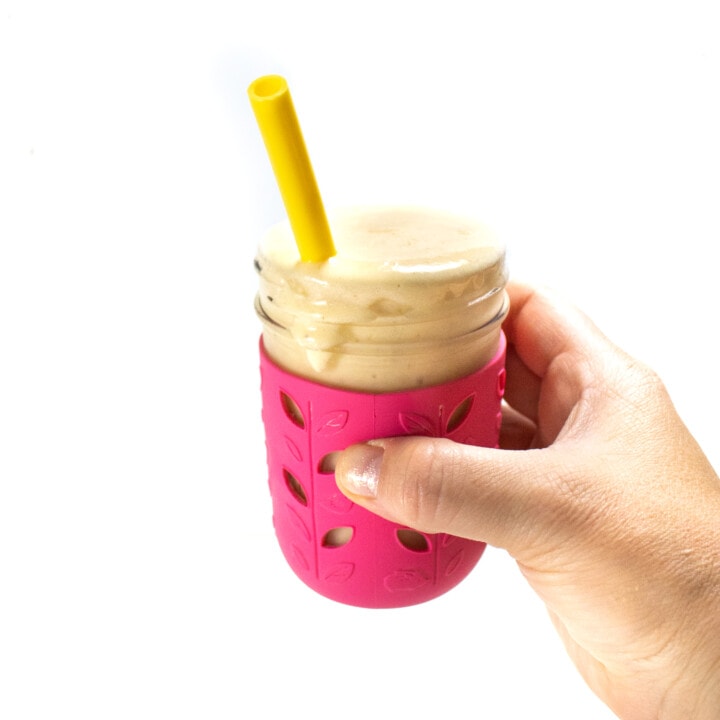 一只手拿着粉红色的冰沙杯，里面装有哈密瓜冰沙和一根黄色的稻草。