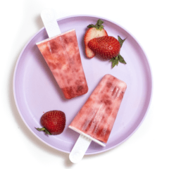 一个紫色的颜色板，上面有两个旋转的草莓酸奶冰棍和在白色背景上切成薄片的草莓。