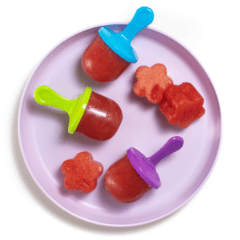 紫色的小孩板，上面有三个西瓜冰棍，上面有五颜六色的冰棒棒和盘子上的大块西瓜在白色背景上。
