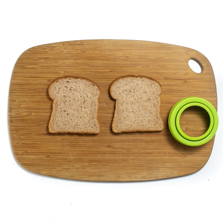 木制切菜板上的两块面包和绿色的三明治切割机。