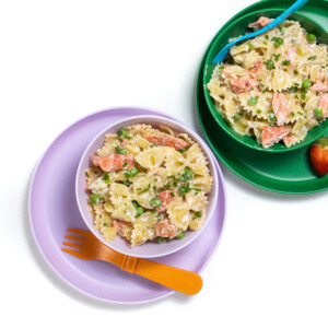 一套紫色和绿色的儿童碗和盘子和鲑鱼面食，里面有豌豆。