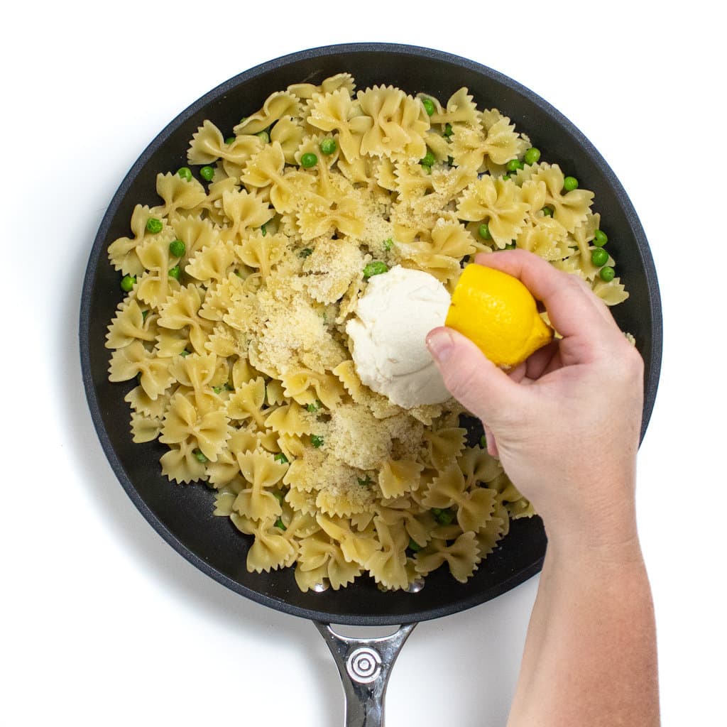 手动将柠檬挤在一个充满意大利面，豌豆，意大利乳清干酪和帕尔玛干酪的熟练的熟练的上。GydF4y2Ba