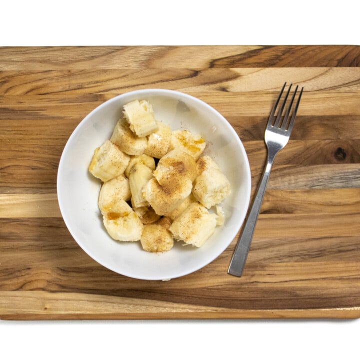 一个带香蕉，肉桂和枫糖浆的切菜板，旁边有叉子。