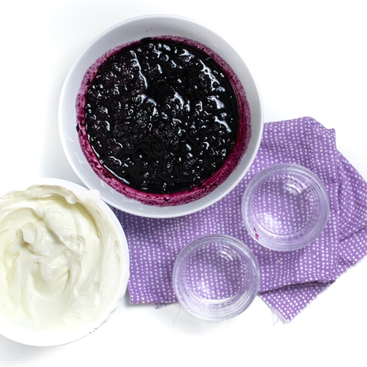 一碗蓝莓蜜饯和酸奶在紫色的餐巾纸上放入白色背景的小罐子中。
