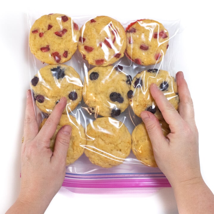 两只手轻轻地从Ziploc袋中轻轻压在Ziploc袋中，上面装满了新鲜制作的自制松饼。