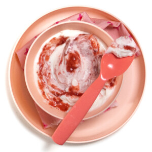 一个装满白色酸奶和草莓泥的粉红色碗和盘子在白色背景上旋转。