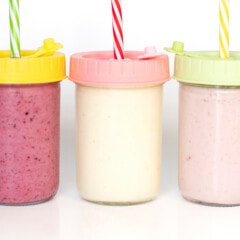可欣赏三个玻璃罐，上面有五颜六色的盖子和为儿童提供酸奶饮料的吸管。