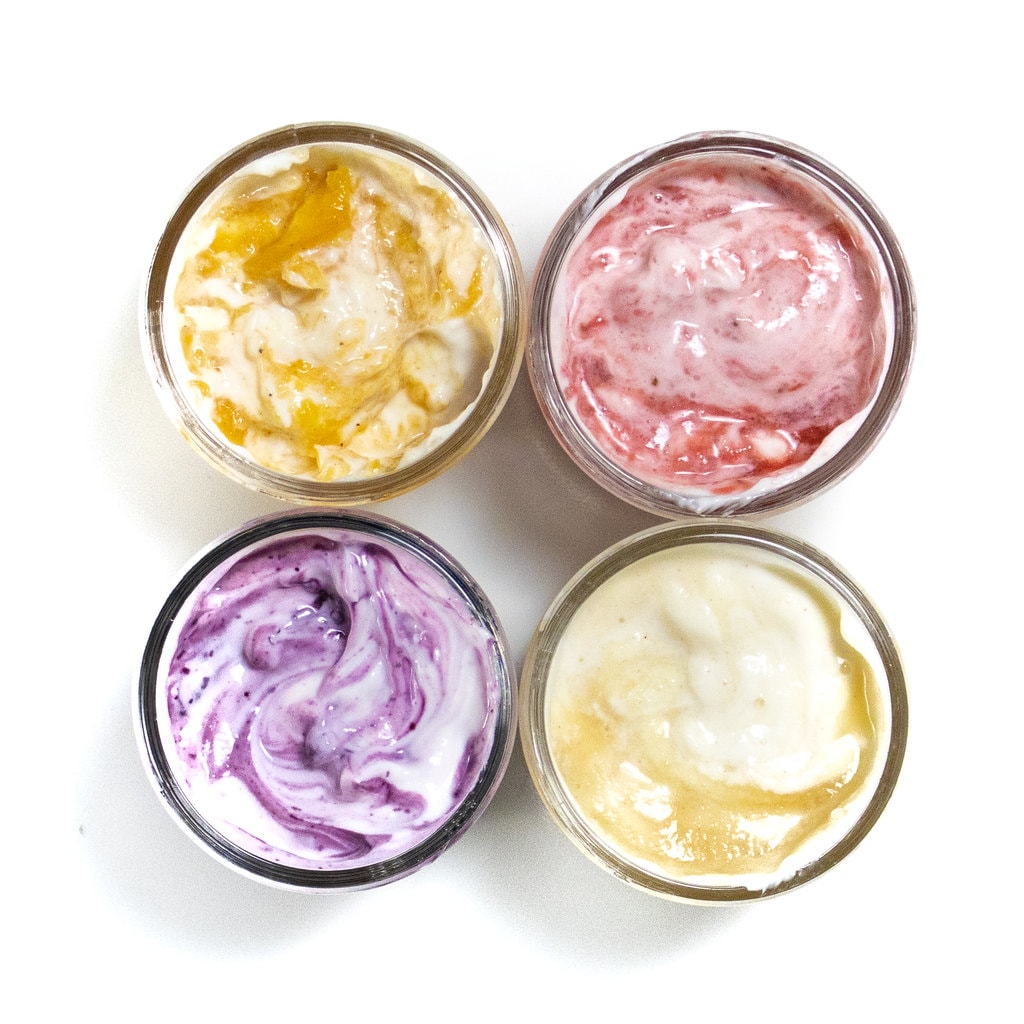 对于装满水果的玻璃罐，旋转着酸奶，并在白色背景下以不同的风味和颜色。