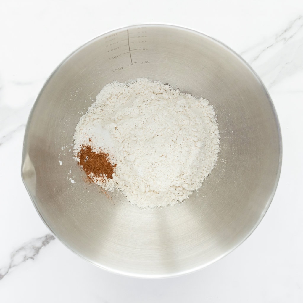 银色的搅拌碗，面粉，发酵粉，盐和肉桂，在大理石柜台上。