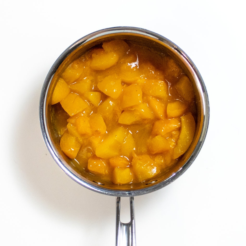 一个小的银酱锅，里面装满了夏季杏子，上面有丁香和水。
