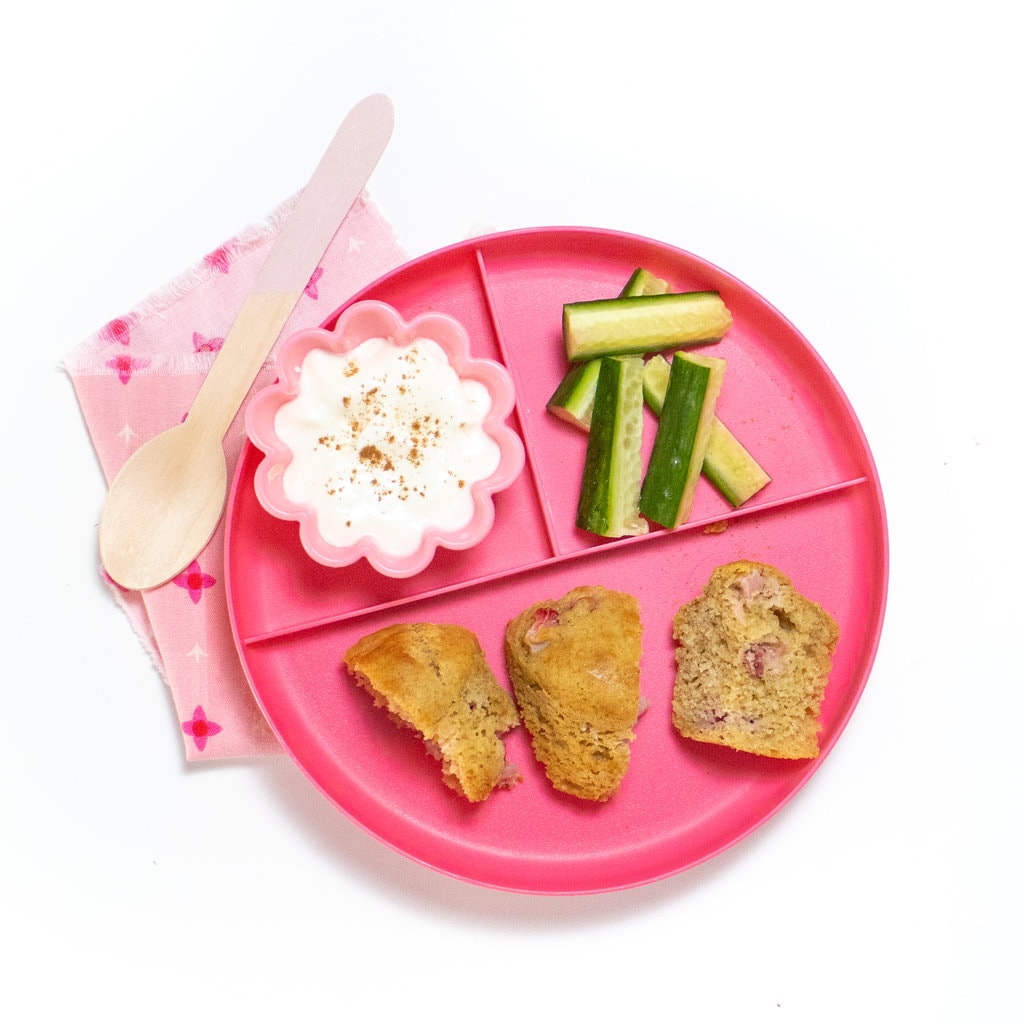 粉红小朋友玩三片, 一只草莓松饼切成三分, 一只黄瓜切成黄瓜, 另一只酸黄瓜上洒肉桂侧面有粉红色木勺和粉红色餐巾