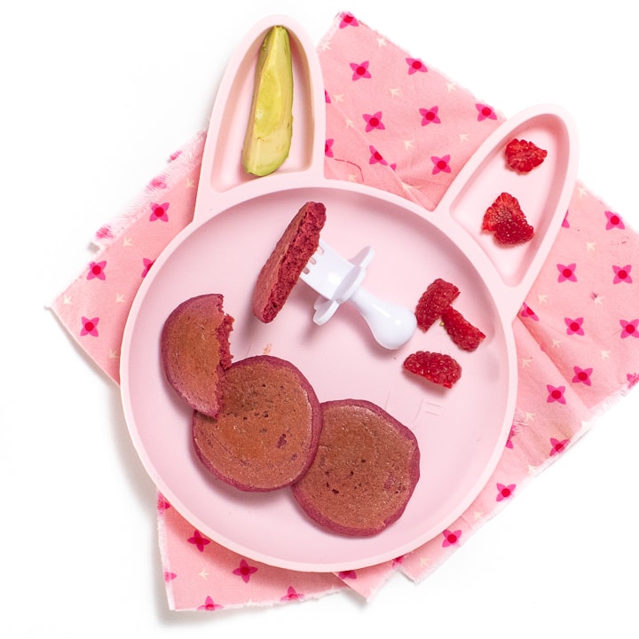 红兔板装满粉红煎饼 树莓和avocado 坐在粉红餐巾上 白叉子供婴儿使用