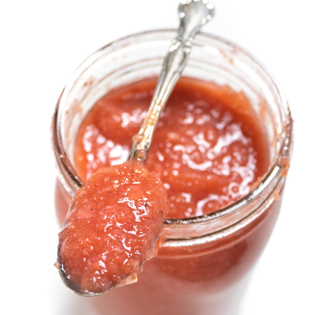 一个装满草莓苹果酱的罐子，上面放着一个银勺，上面装满了草莓苹果酱。GydF4y2Ba