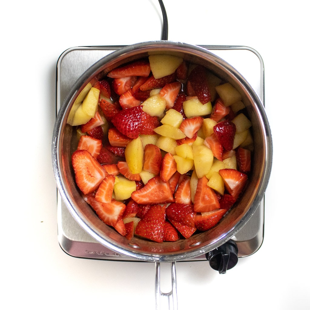 一个银酱锅，切碎的苹果和草莓烹饪。GydF4y2Ba