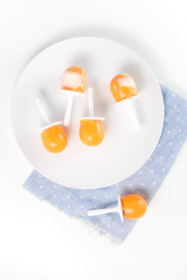 圆白板顶部蓝餐巾盘子上有四片橙式冰棒 内有酸奶旋转餐巾上有一个橙色冰棒