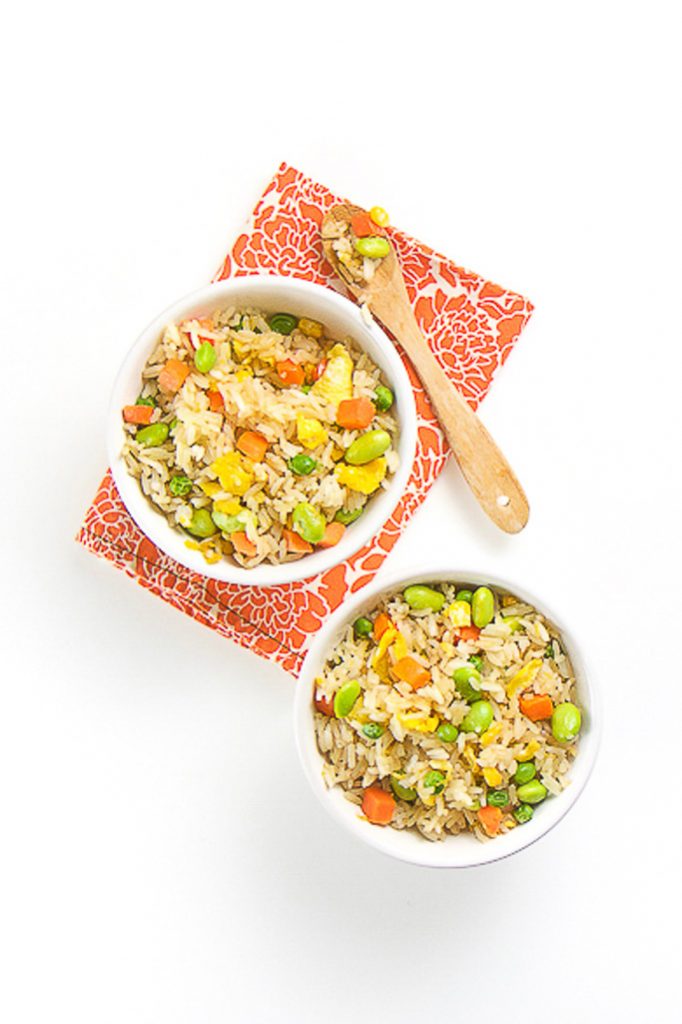 2个白碗装满棕米、蔬菜和炒鸡蛋块碗坐在橙花板上碗顶上有木勺子 饭加进