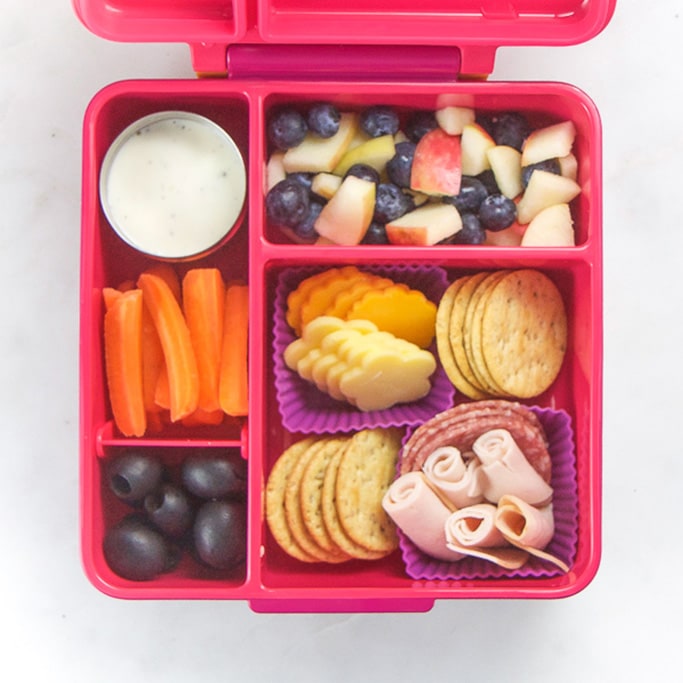 粉红色的学bob平台校午餐盒，里面充满了健康，简单的学校午餐想法 - 奶酪，饼干，水果和胡萝卜和牧场。