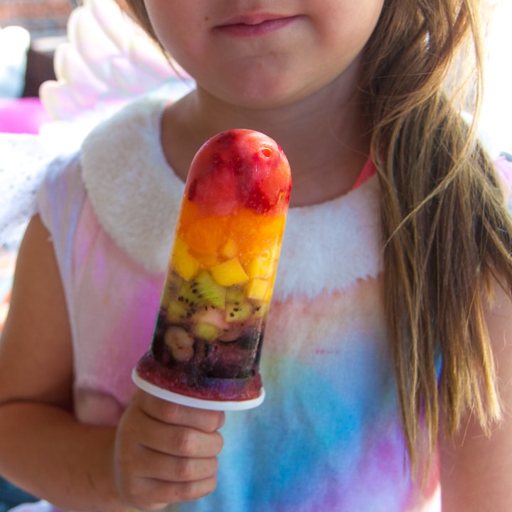 年轻女孩拿着彩虹冰棒穿着彩虹连衣裙。