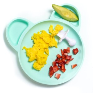 蓝绿色盘子和婴儿早餐 - 炒鸡蛋，鳄梨和切碎的草莓。