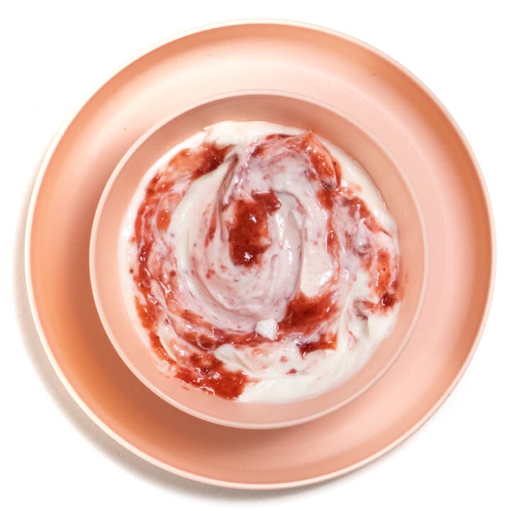 粉红色的儿童盘子和碗在碗内用粉红色的勺子，是酸奶和草莓泥。