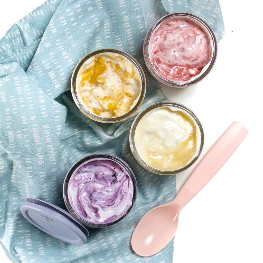 满满酸奶的四杯罐子上方旋转果实,蓝餐巾、粉红勺子和蓝盖白后台