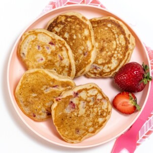 草莓煎饼堆放在粉红孩子盘上 粉红色叉子停在粉红餐巾上